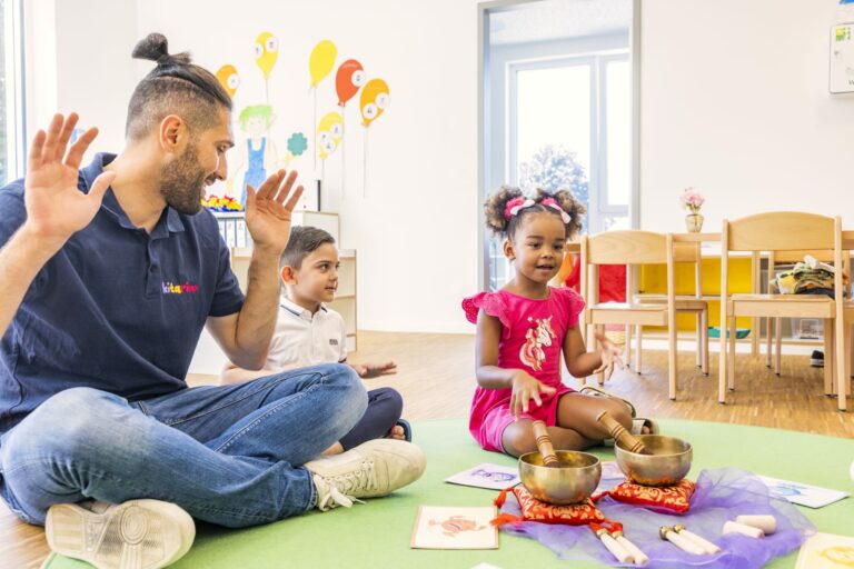 Kitarino Erzieher sitzt mit den Kinder und Klangschalen am Boden