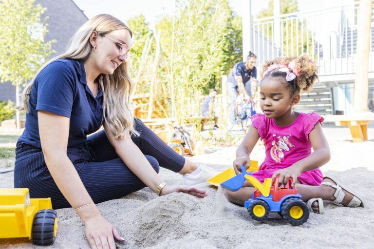 Erzieherin spielt mit Kind im Sand Kitarino