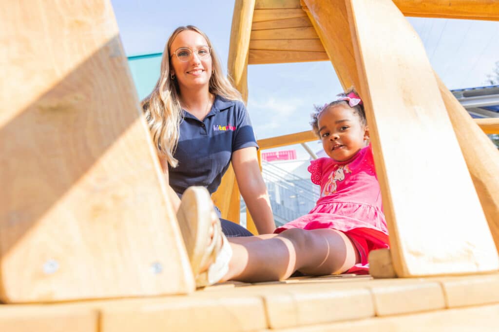 Kind sitzt mit Erzieherin draußen am Spielturm